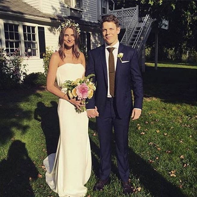 Lauren Deleo in a white bridal dress holding a flower bouquet with her husband in a navy blue suit.